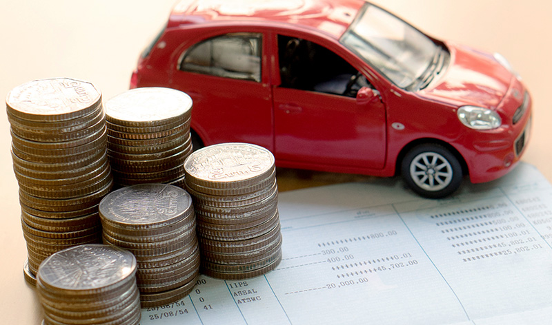 A red toy SUV is sitting beside several stacks of silver coins and all are on top of a sales agreement.